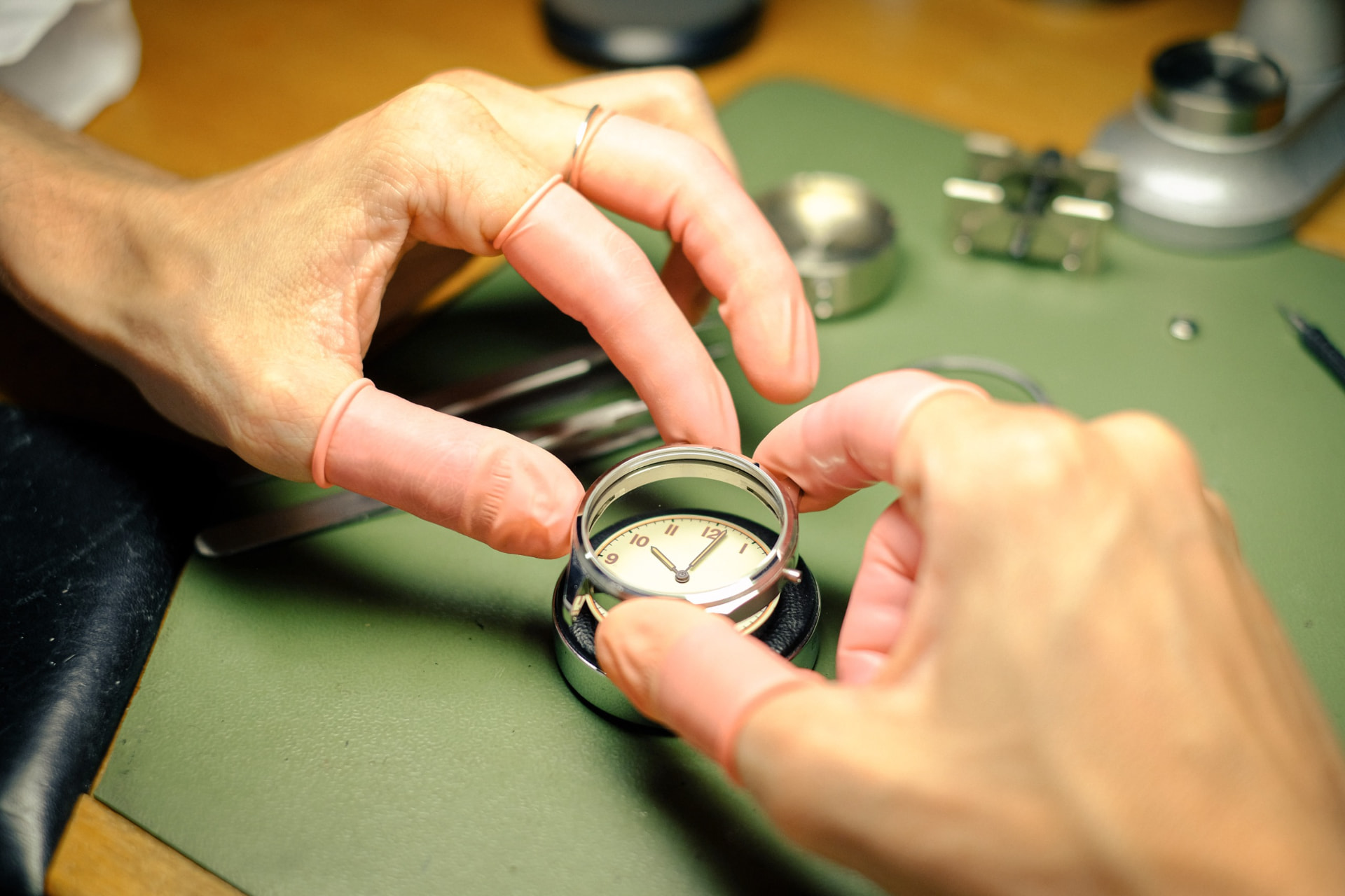 Les mains d'un horloger posant un verre sur un boîtier de montre à l'établi